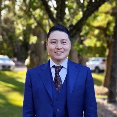 Dr Steven Ma smiles outdoors in a blue suit, a certified sclerotherapist at Dermatology & Vein Institute Australia.