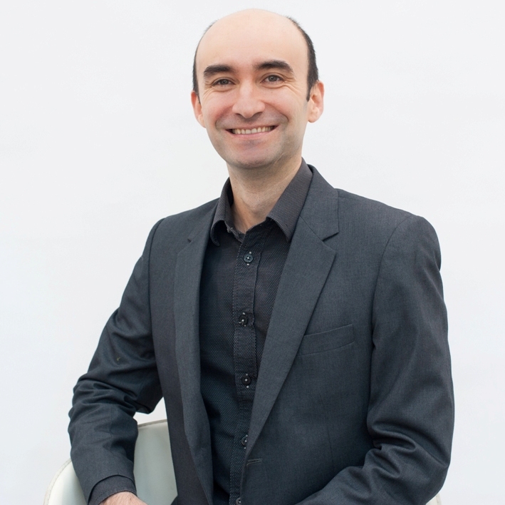 Smiling Dr Gilberto Moreno Bonilla stands in a dark suit against a clean white background at Dermatology & Vein Institute Australia.